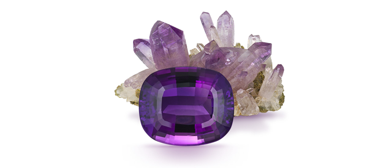 This 22.62 carat (ct) cushion cut amethyst birthstone stands before a cluster of amethyst crystals.