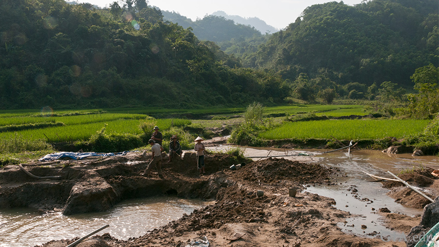 The August birthstone is found in the landscape of Vietnam’s Luc Yen region. A ruby and spinel mining operation is in the foreground, with rice paddies rolling behind it against mountains cloaked in trees.