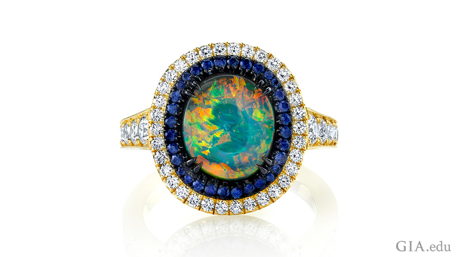 Sapphires and diamonds encircle the October birthstone, a 1.92 carat black opal in a stunning 18K yellow gold and black rhodium ring.
