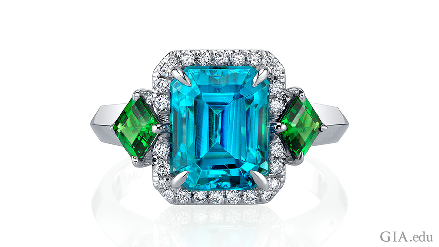 Handcrafted December birthstone ring with a 6.59 carat emerald cut blue zircon center stone accented by emerald cut tsavorite garnets, and brilliant diamond rounds set in 18K white gold.